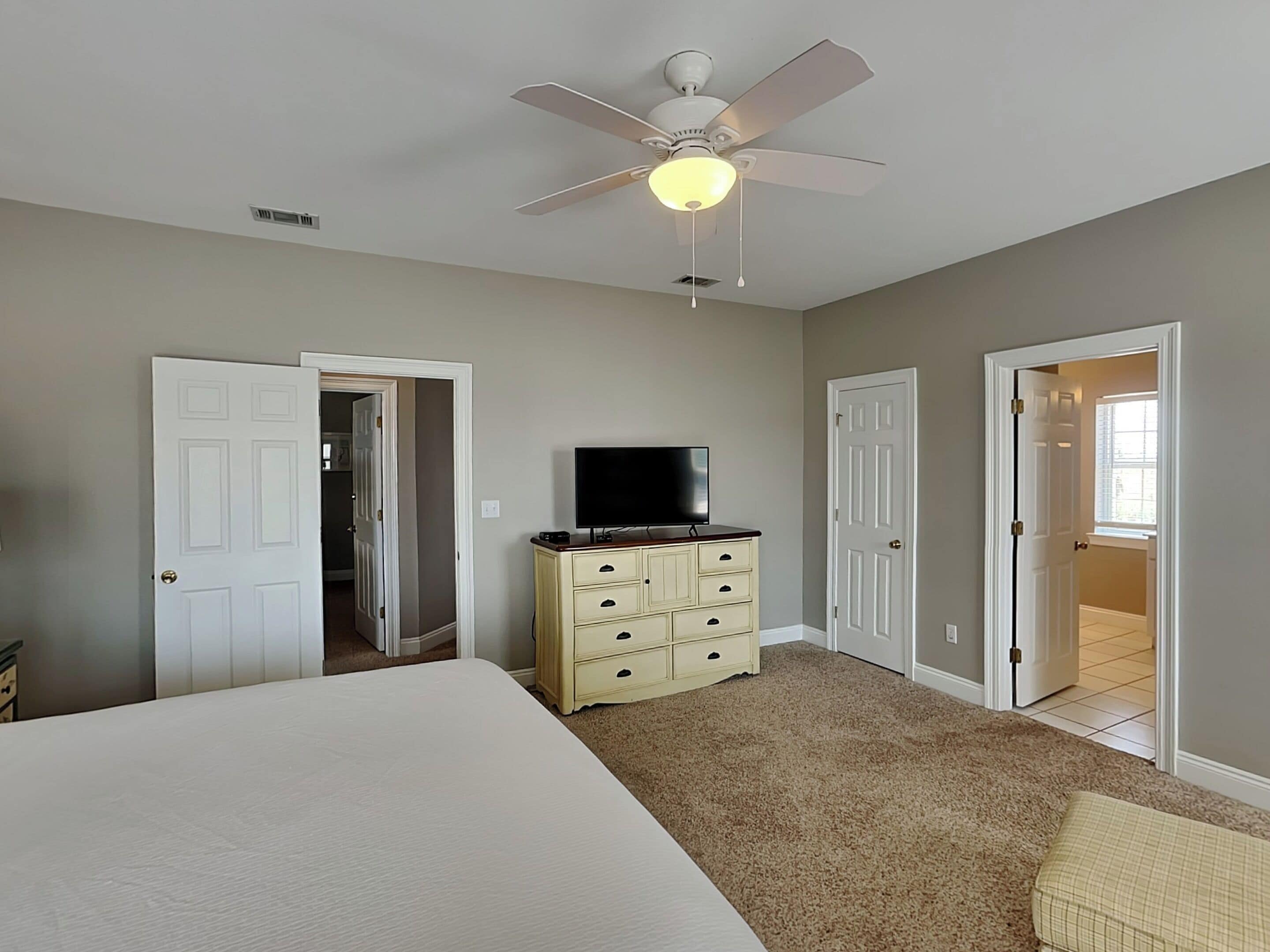 A bedroom with a bed, a dresser, a ceiling fan, and a TV.