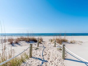 A sandy beach path leading to the ocean, bordered by wooden posts and rope barriers.