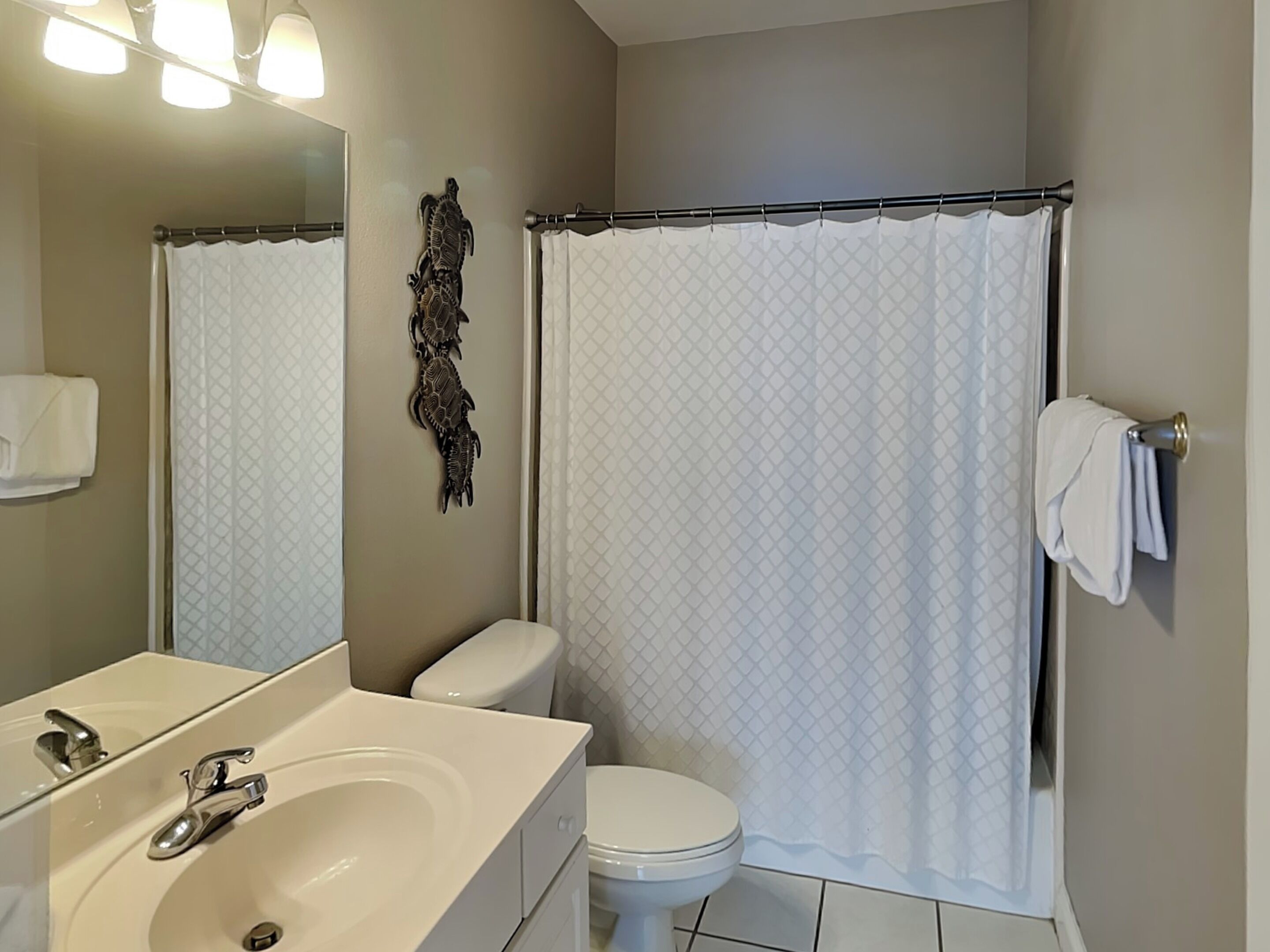 Un bagno con lavandino, water e tenda per la doccia, tutto in bianco.