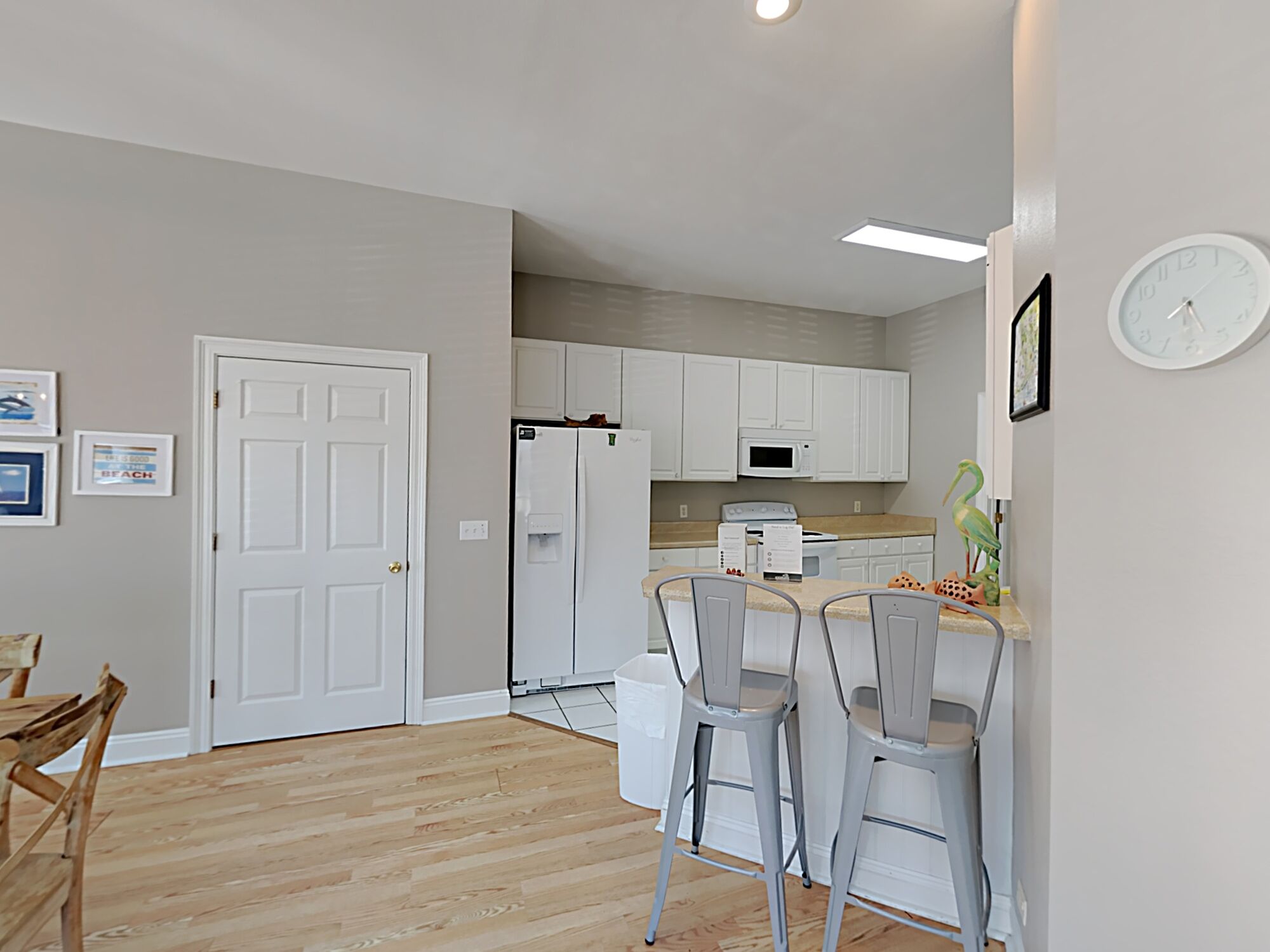 A modern kitchen with white cabinets, a refrigerator, a microwave, and a dining area with two bar stools.