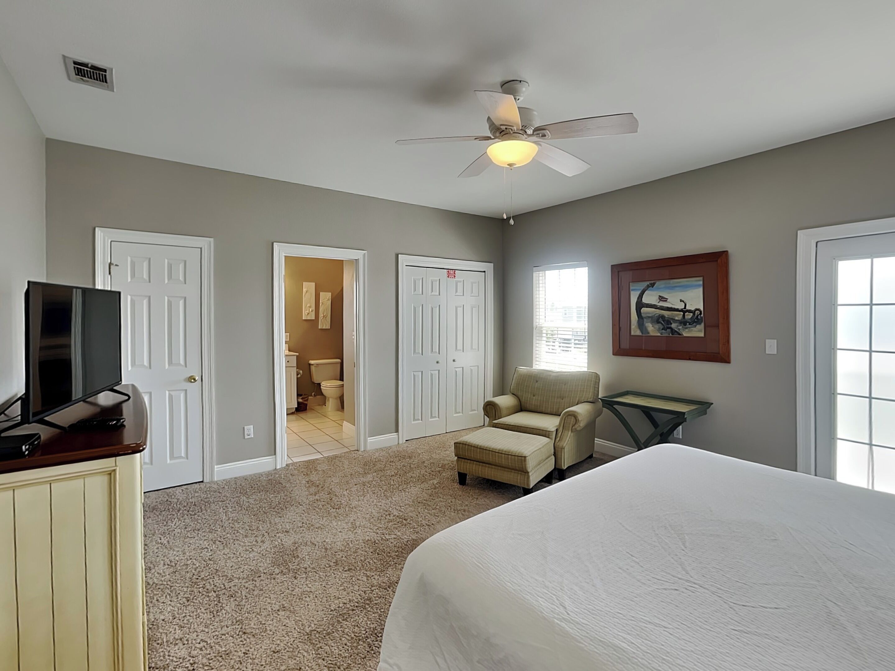 A bedroom with a bed, a chair, a desk, a television, and a ceiling fan.