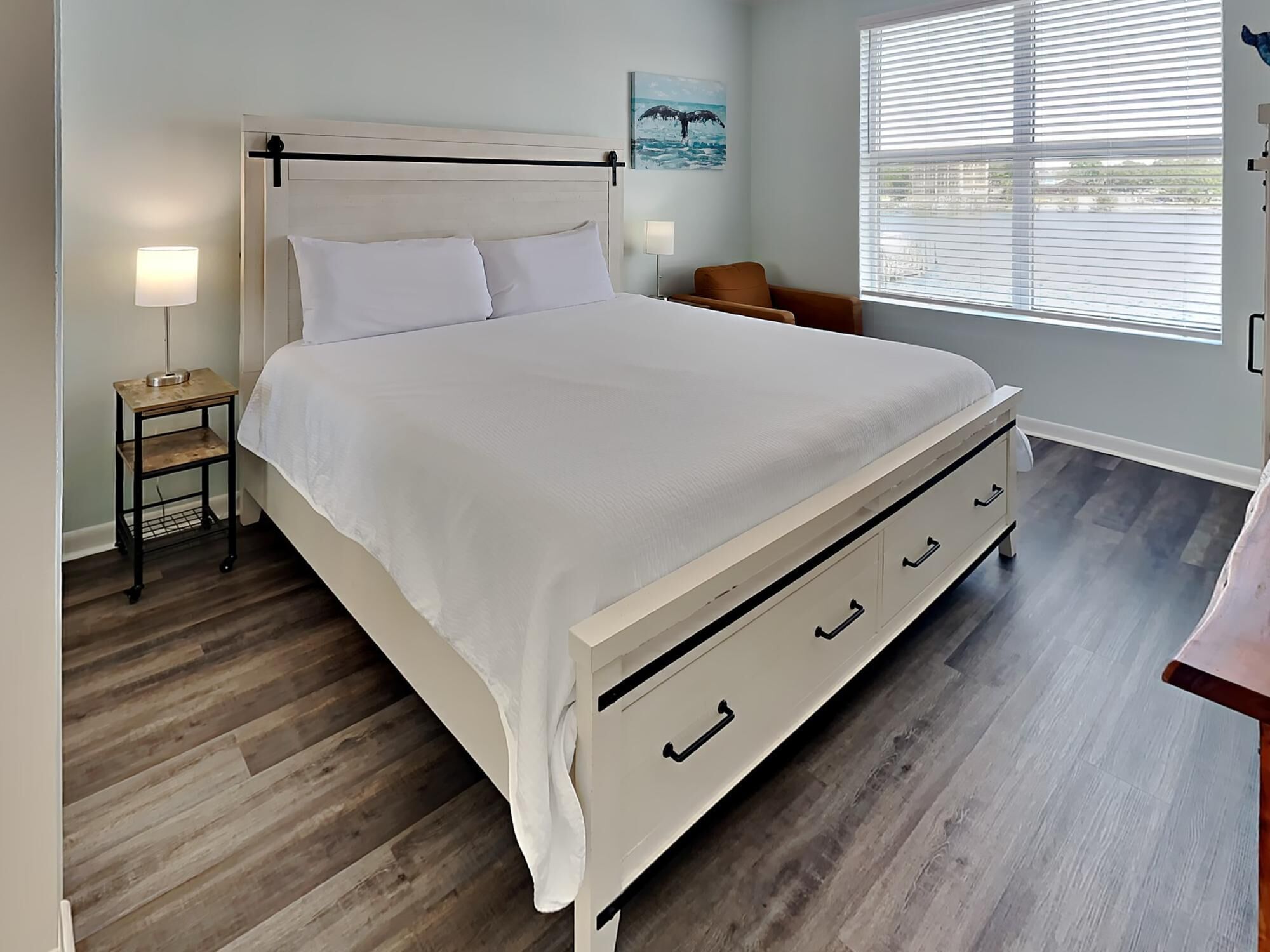 A bed with a wooden headboard, white bedding, and a nightstand with a lamp.