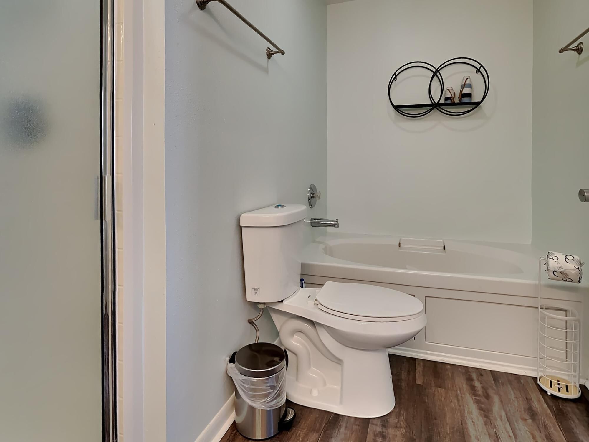Un bany amb vàter, bidet i banyera. Hi ha un cubell de brossa i un penjador de tovalloles a la paret.
