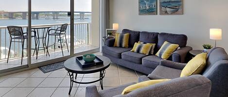A modern living room with a grey sofa, a coffee table, and a balcony with a view of a bridge.