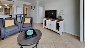 Una sala de estar con un sofá gris, una mesa de centro con un cuenco, un televisor sobre un mueble blanco y un reloj en la pared.