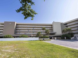 Un hotel de varios pisos con fachada plana, balcones y un estacionamiento.
