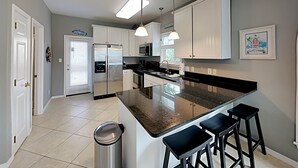 Eine moderne Küche mit weißen Schränken, einem Edelstahl-Kühlschrank, einer großen Kochinsel mit Barhocker und Pendelleuchten.