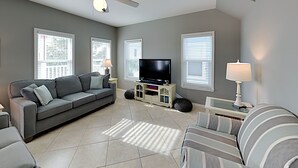 Ein Wohnzimmer mit grauem Sofa, einem gestreiften Sessel, einem Fernseher und einem Deckenventilator.