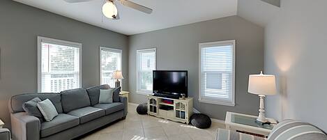 A living room with a grey sofa, a striped armchair, a TV, and a ceiling fan.
