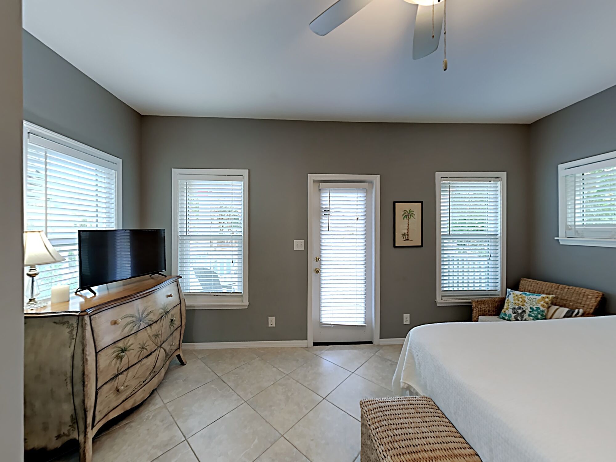 A bedroom with a bed, dresser, TV, and windows.