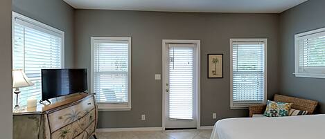 A bedroom with a bed, dresser, TV, and windows.