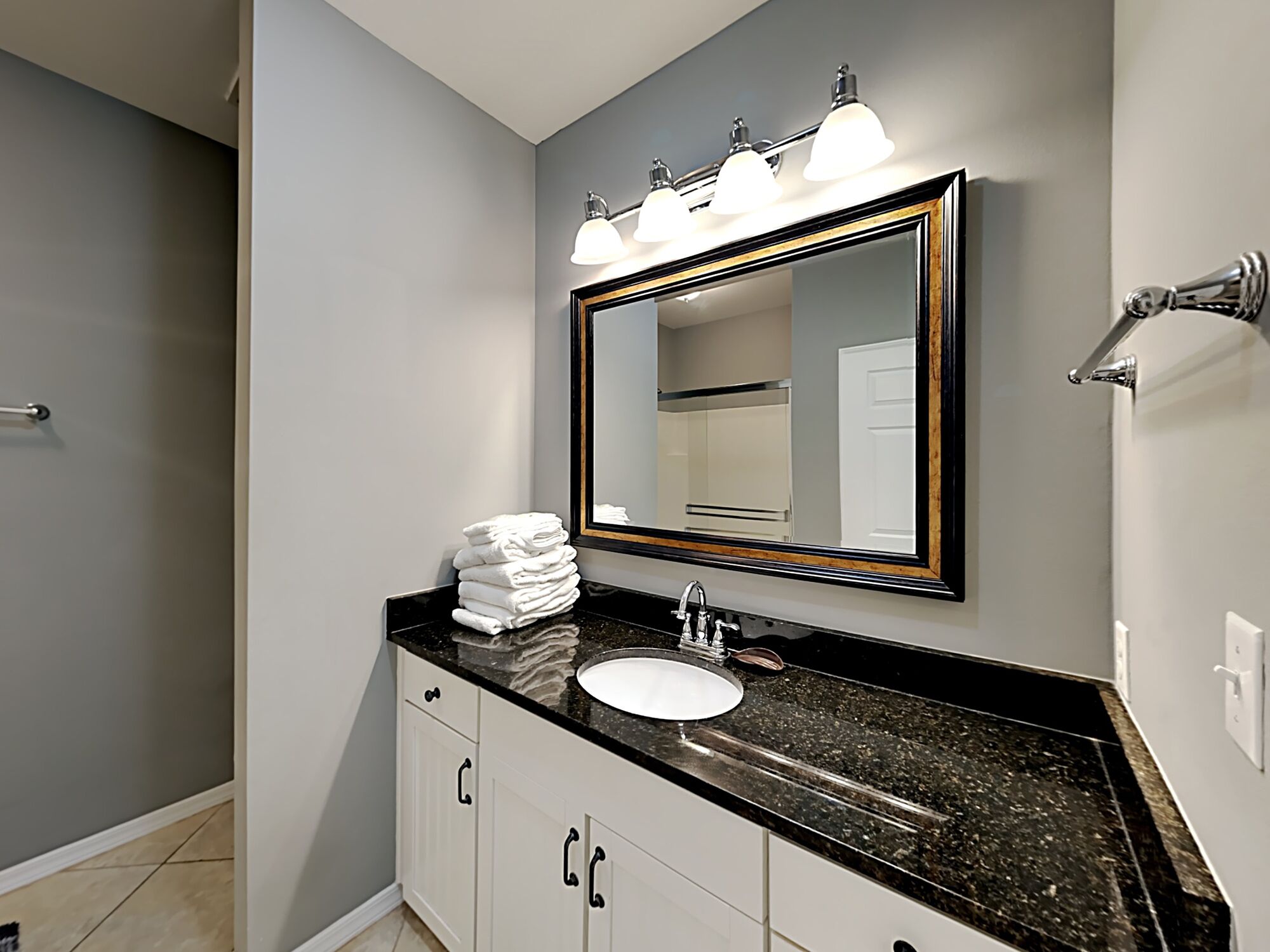 A bathroom with a black granite countertop, white cabinets, a white sink, and a mirror with lights above it.