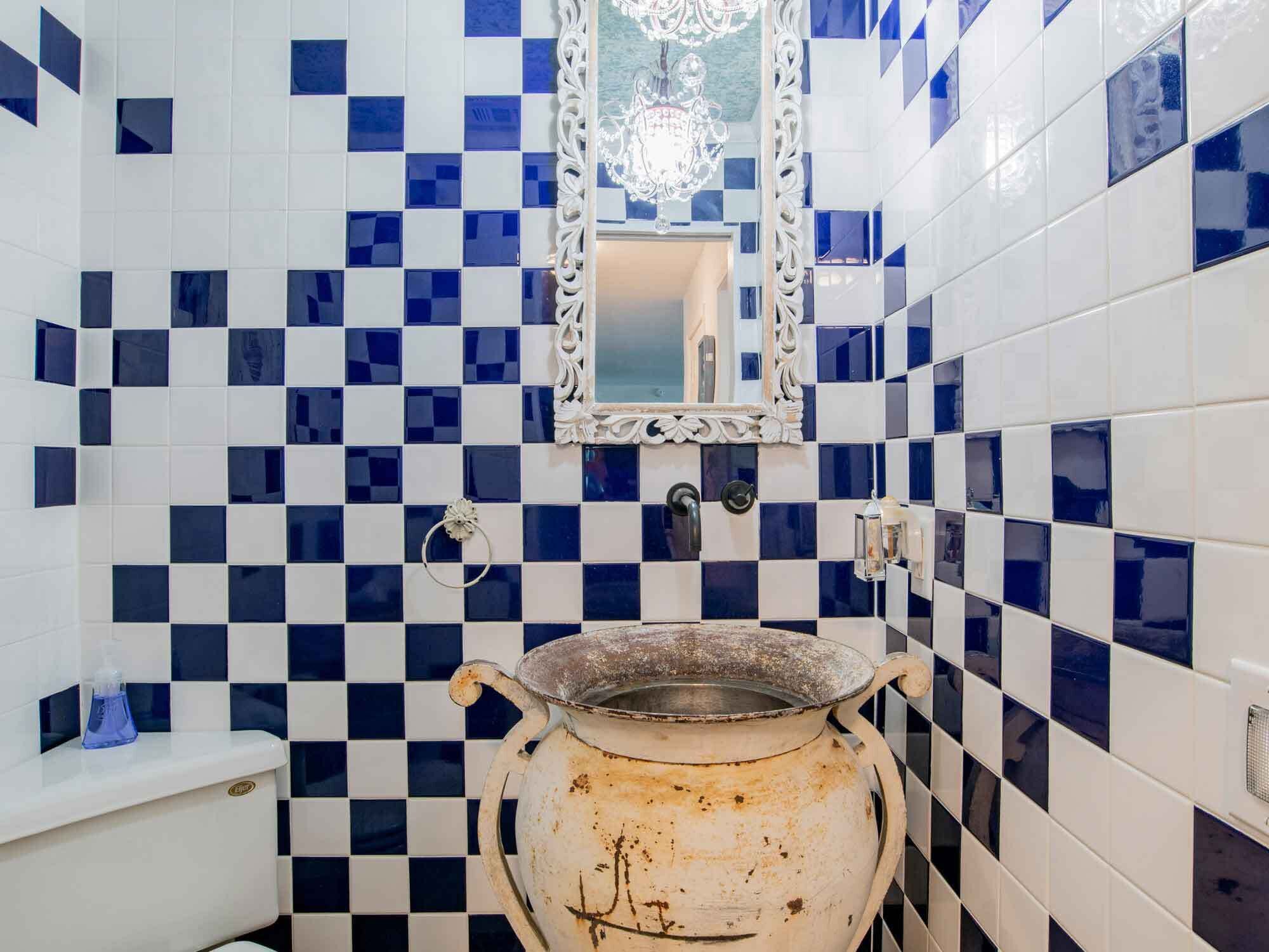 A bathroom with blue and white checkered tiles, a white sink, a mirror, and a large, rustic, white pot.