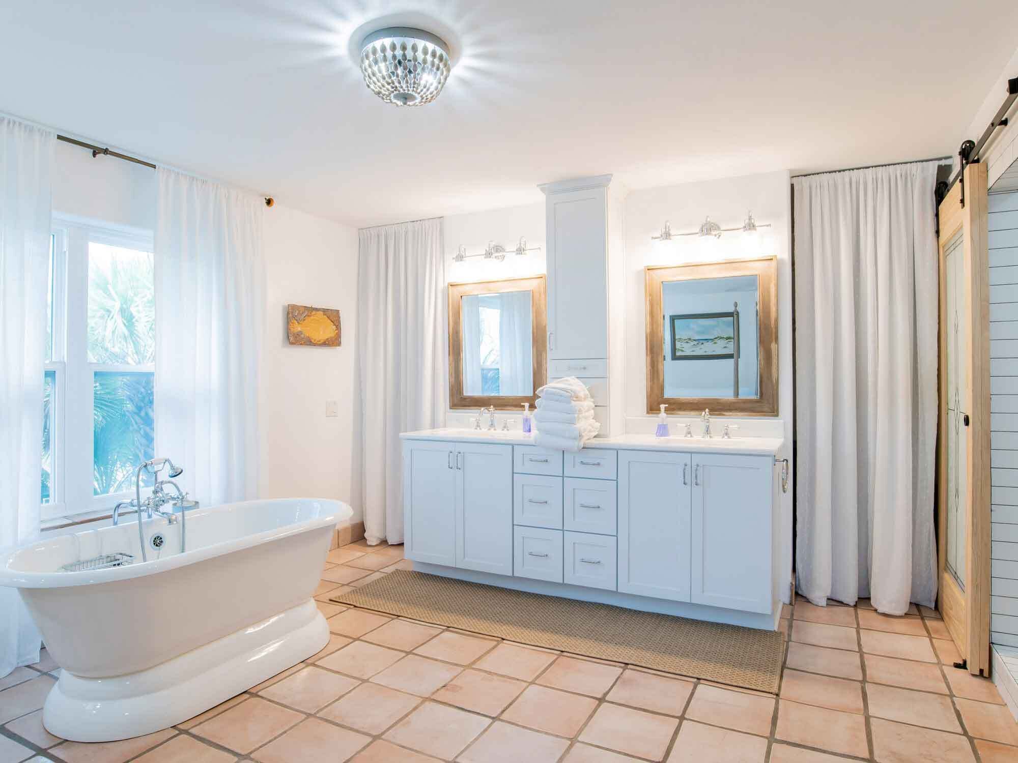 A bathroom with a freestanding bathtub, a double vanity with two mirrors, and a chandelier.