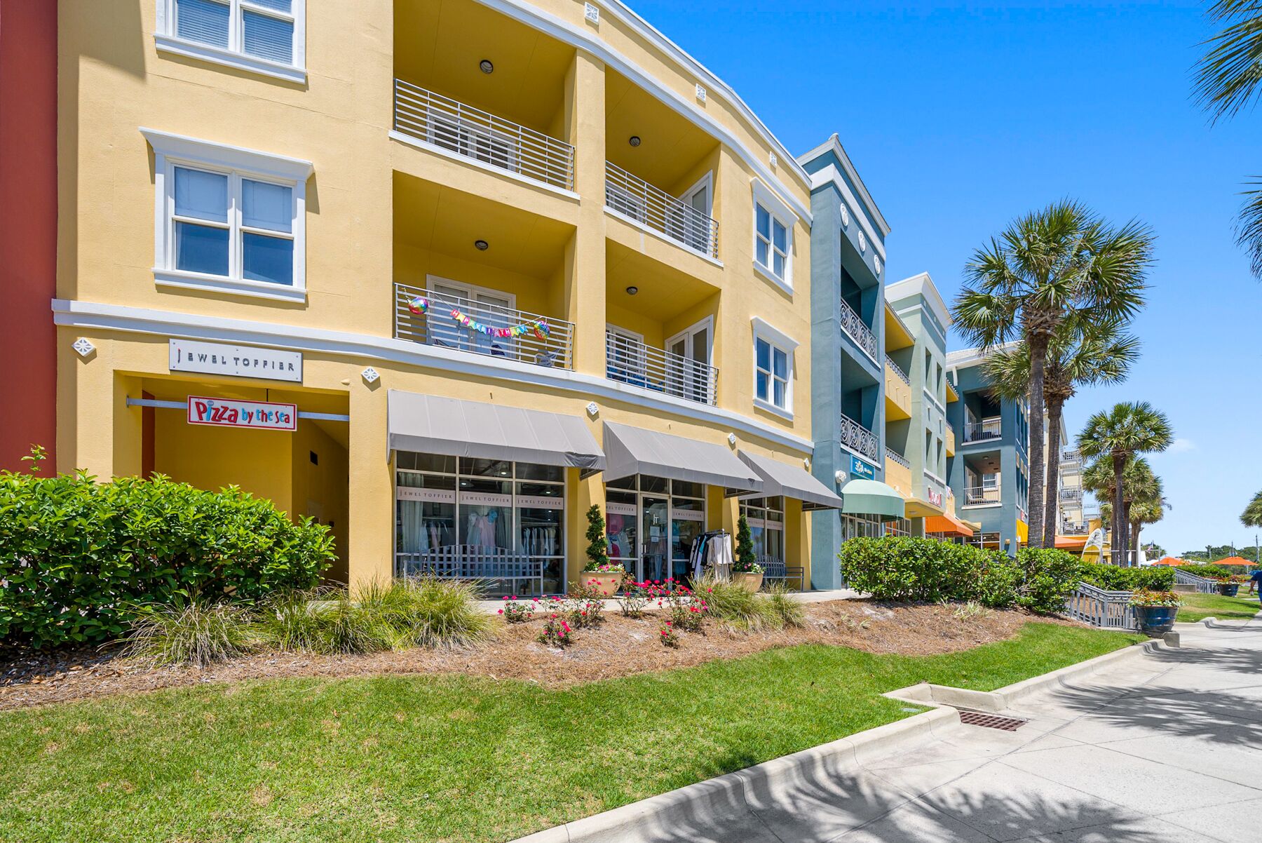 A multi-story yellow building with a ground-level restaurant named "Pizza by the sea" and a visible store named "Jewel Toppler."