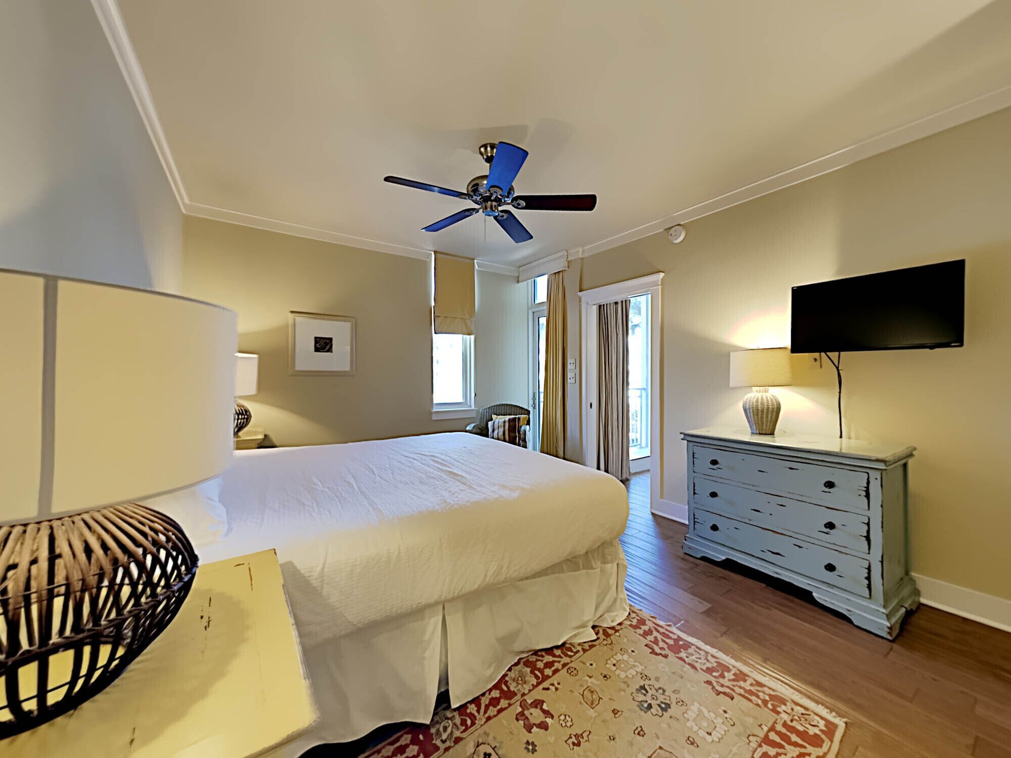 A bedroom with a bed, a ceiling fan, a dresser, a TV, and a window.