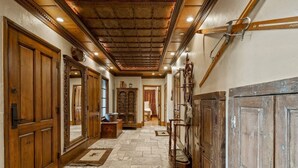 A hallway with wooden doors, a stone floor, and a ceiling with exposed beams. - 5 Beds in BC - Ski In, Hot Tub, Pool (Beaver Creek)