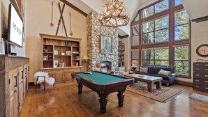A spacious room with a pool table, a fireplace, and a large window offering a view of trees. - 5 Beds in BC - Ski In, Hot Tub, Pool (Beaver Creek)