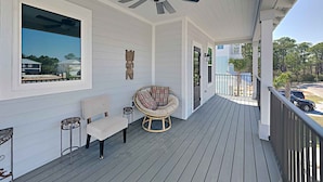 A covered porch with a ceiling fan, a wicker chair, a cushioned bench, and a view of the surrounding neighborhood. - Sunshine Vacation Home by Southern Vacation Rentals (Miramar Beach)