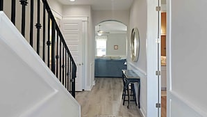 A hallway with a staircase, a dining area with a blue sofa, and a large mirror on the wall. - Sunshine Vacation Home by Southern Vacation Rentals (Miramar Beach)