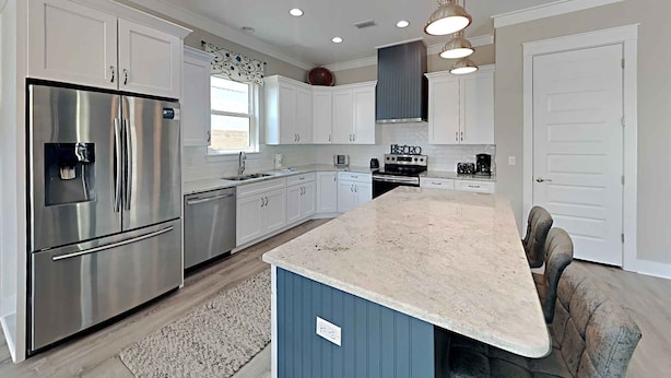 A modern kitchen with white cabinetry, a stainless steel refrigerator, a built-in oven, and a granite countertop island. - Sunshine Vacation Home by Southern Vacation Rentals (Miramar Beach)