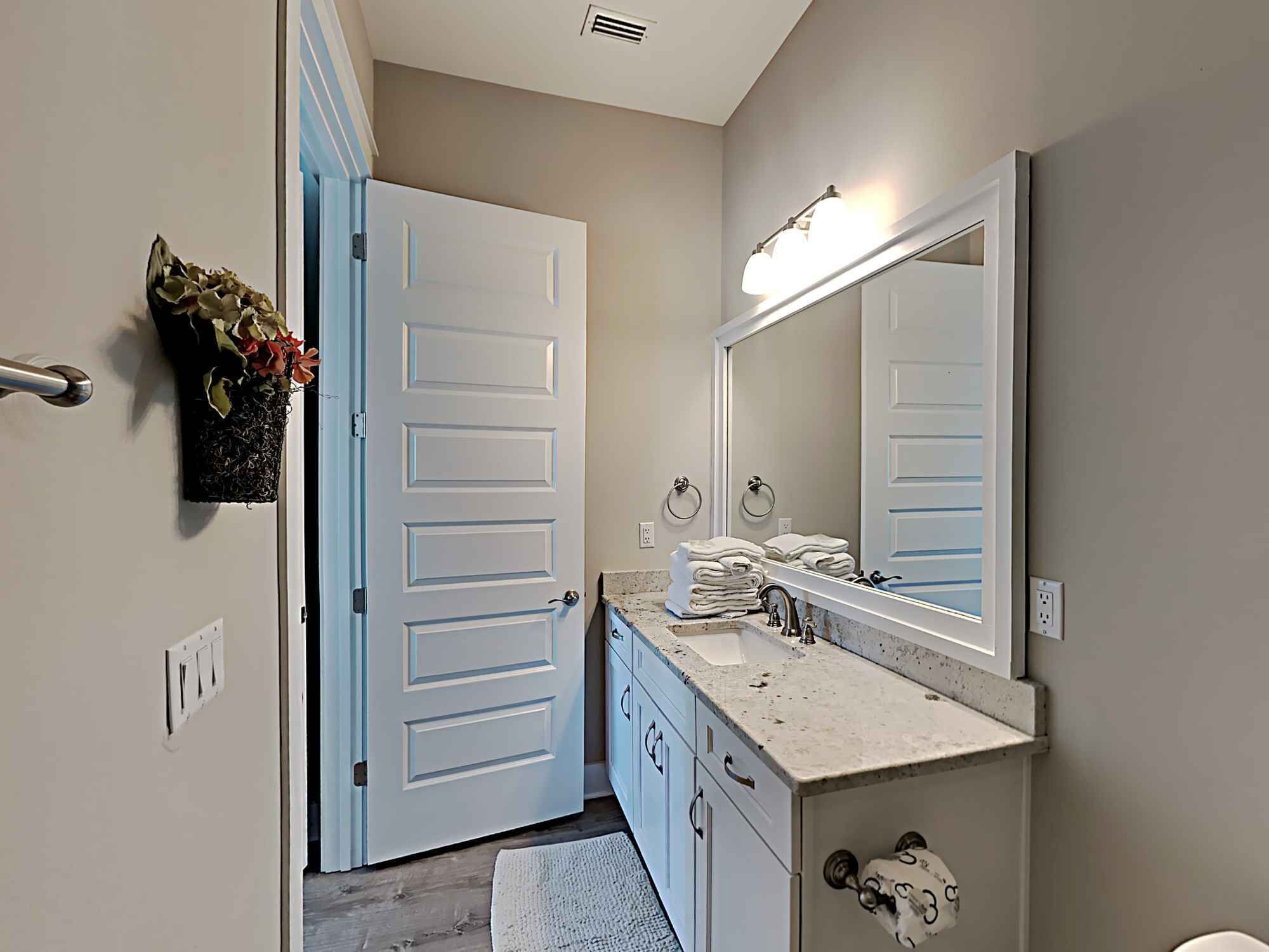 Casa de banho com porta branca, pia com espelho e um porta-toalhas.