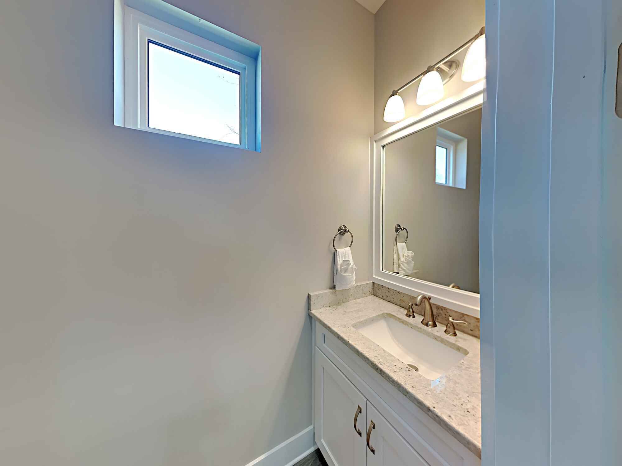 A bathroom with a window, a sink with a mirror, and a towel rack.