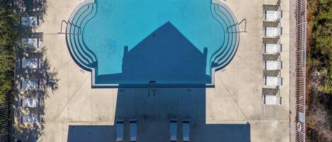 An aerial view of a swimming pool with a geometric design, surrounded by a fence and multiple seating areas.