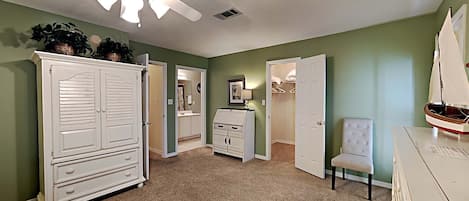 A room with a ceiling fan, a white wardrobe, a small white chair, and a sailboat model on a dresser.
