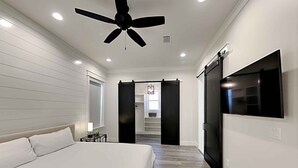 Quarto com cama, ventilador de teto, televisão e porta deslizante que dá para um closet.