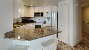 A modern kitchen with white cabinets, a granite countertop, stainless steel appliances, and a built-in island with bar stools. - Phoenix X by Southern Vacation Rentals (Orange Beach)
