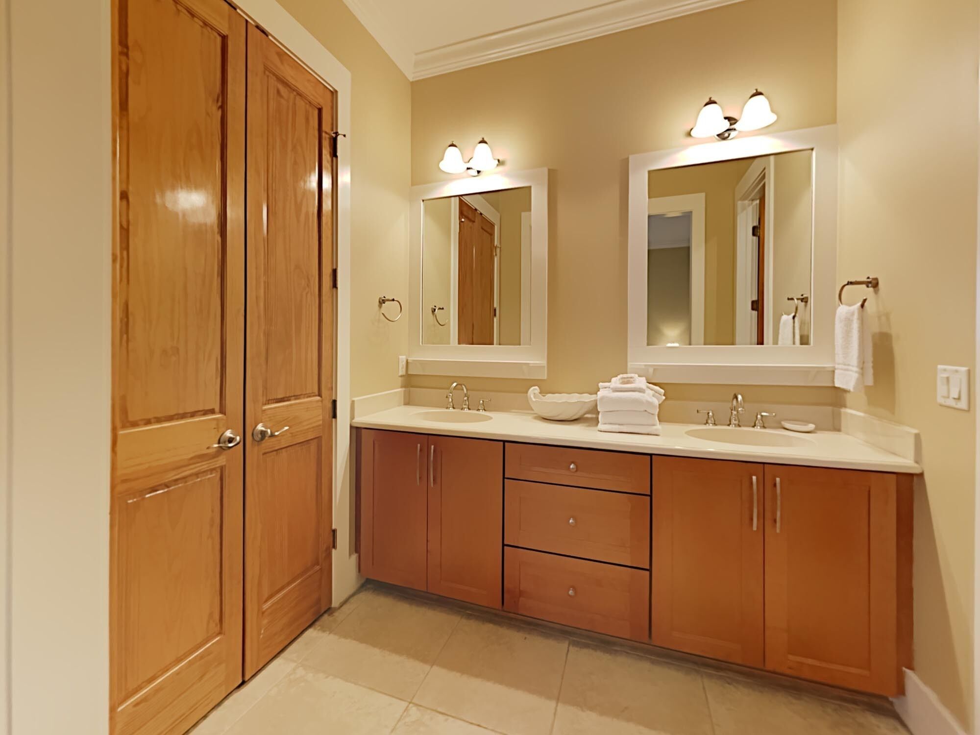A bathroom with wooden cabinets, a double sink, and a large mirror with lights.