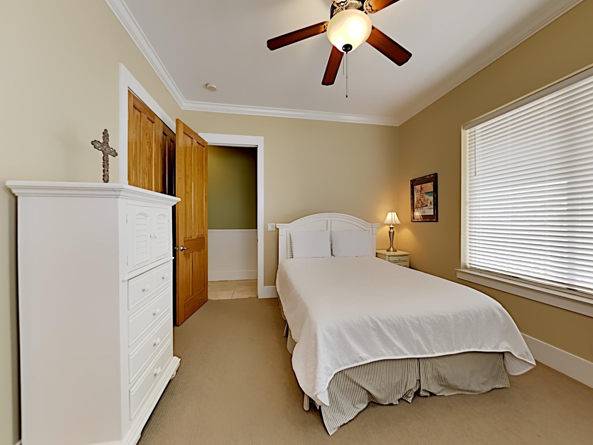 A bedroom with a bed, a nightstand, a lamp, a ceiling fan, and a wardrobe.