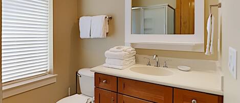 A bathroom with a toilet, sink, mirror, and wooden cabinets.