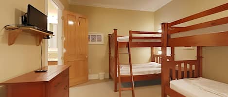 A bedroom with bunk beds, a wooden dresser, a ceiling fan, and a TV on a shelf.