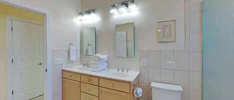 A bathroom with a double sink vanity, a toilet, and a trash bin.
