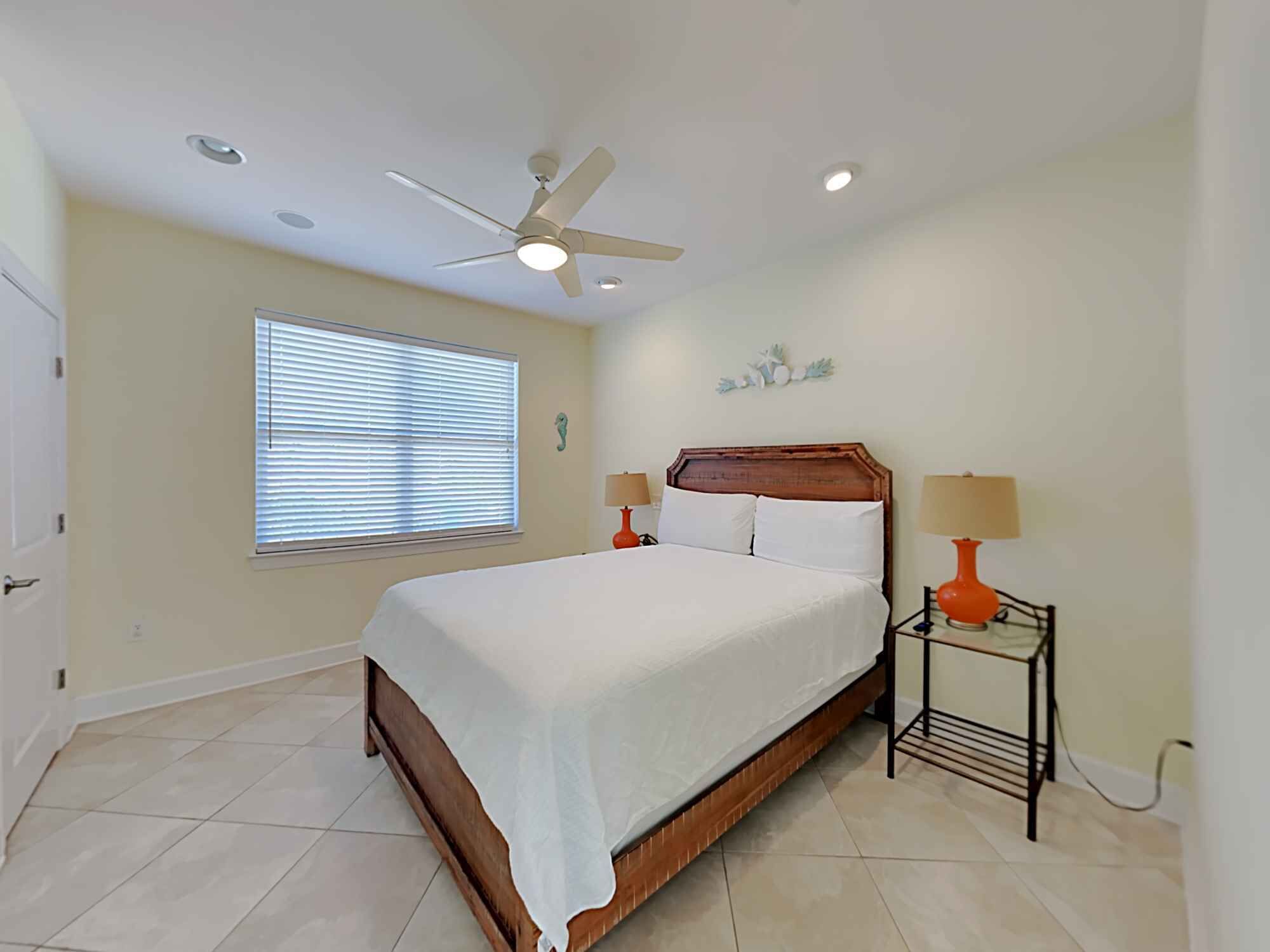 A bedroom with a bed, ceiling fan, window with blinds, and two bedside lamps.