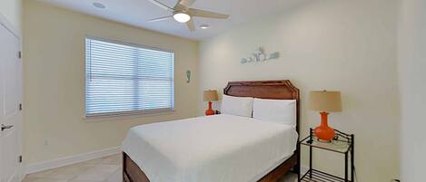 A bedroom with a bed, ceiling fan, window with blinds, and two bedside lamps.