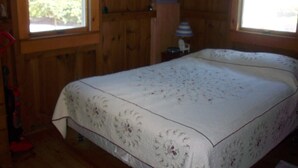 A wooden cabin room with a bed, a nightstand, and a window with a view of greenery outside. - Walk to popular Mayflower Beach in Dennis MA  (Dennis)