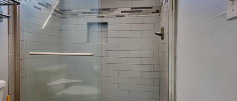 A glass-enclosed shower with a white tiled wall, a glass door, and a small window above the shower.