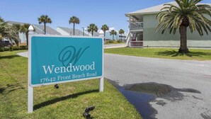 A sign for 'Wendwood' at 17642 Front Beach Road, with a building and palm trees in the background. - Wendwood #E1 by Resort Collection (Panama City Beach)