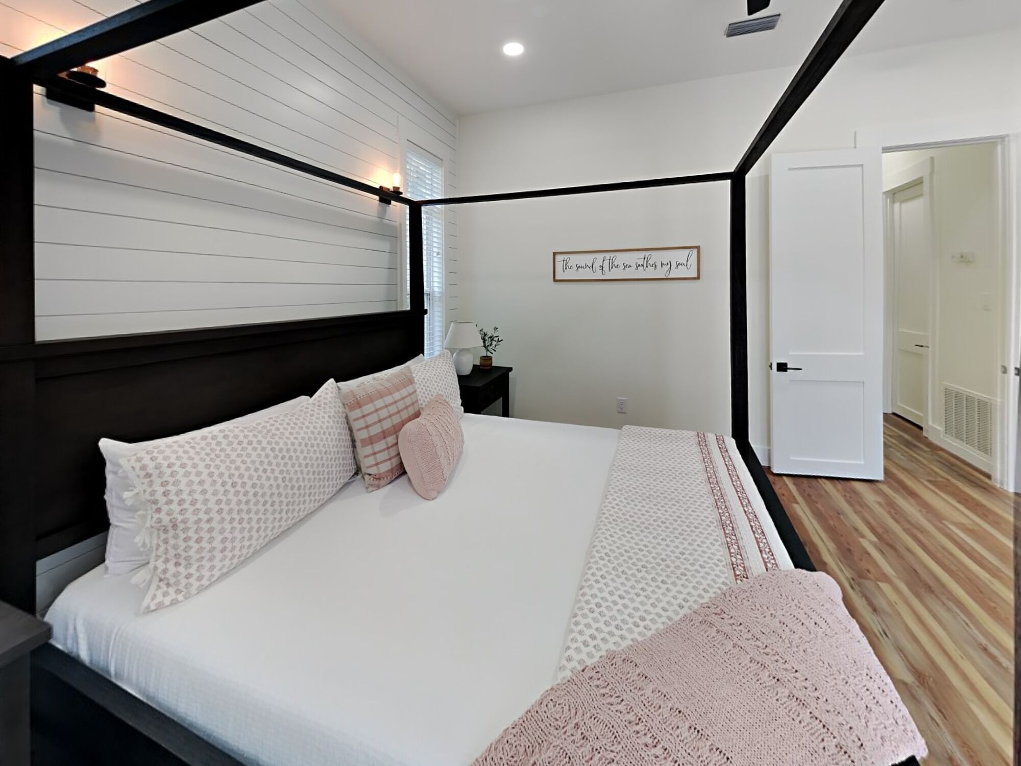 Una cama bien hecha con almohadas estampadas y una manta tejida, una lámpara de noche y una pared con una cita enmarcada.