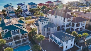Ett flygbildsfoto av ett bostadsområde vid kusten med flera hus, en swimmingpool och palmer.