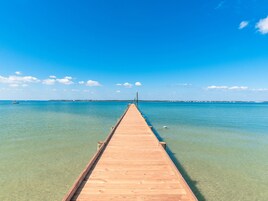 Un muelle de madera que se adentra en aguas azules y transparentes, con una costa distante.