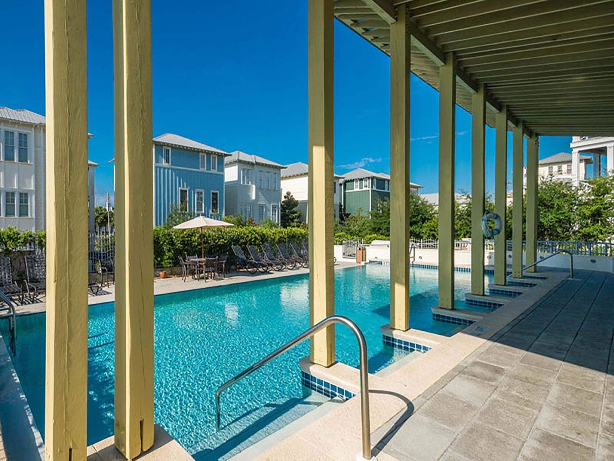 A pool area with clear blue water, lounge chairs, and a covered walkway.