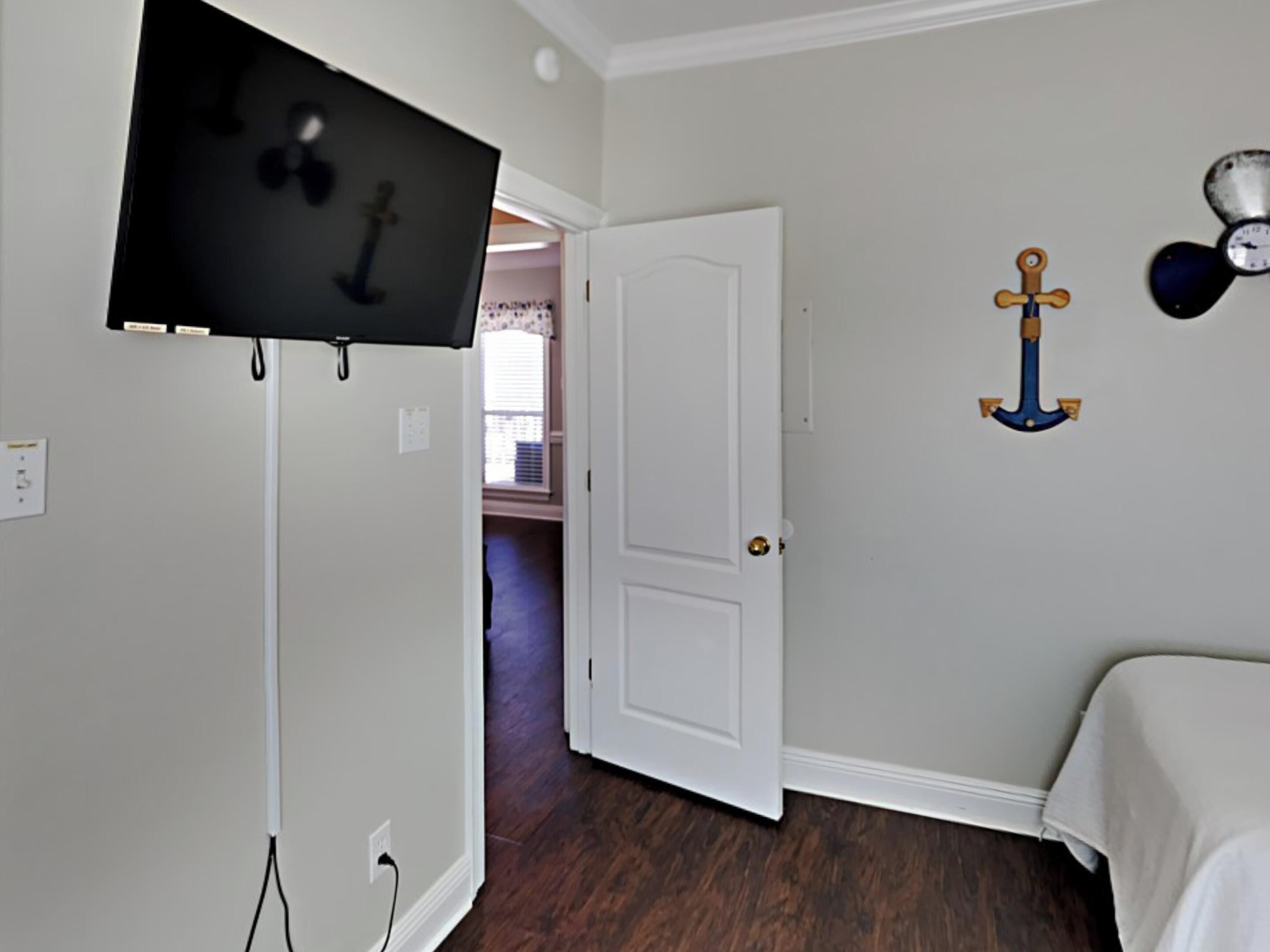 Une pièce avec un téléviseur fixé au mur, une porte blanche et un lit recouvert d’une couverture blanche.