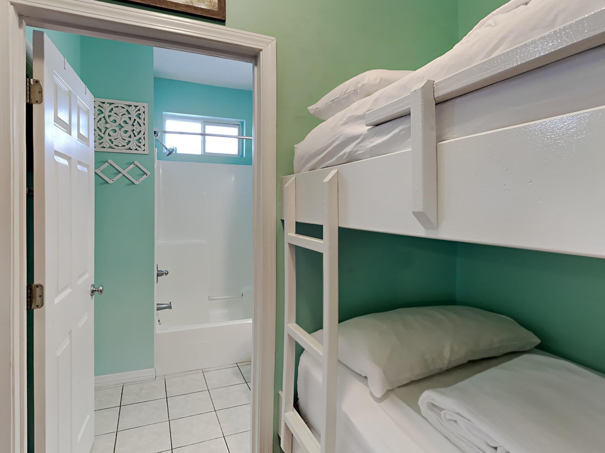 Une chambre avec des lits superposés, une salle de bain avec une baignoire et une porte donnant sur une autre pièce.