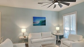 A living room with a ceiling fan, a painting of a wave, two lamps, and a window with blinds. - A Sun of a Beach by Southern Vacation Rentals (Miramar Beach)
