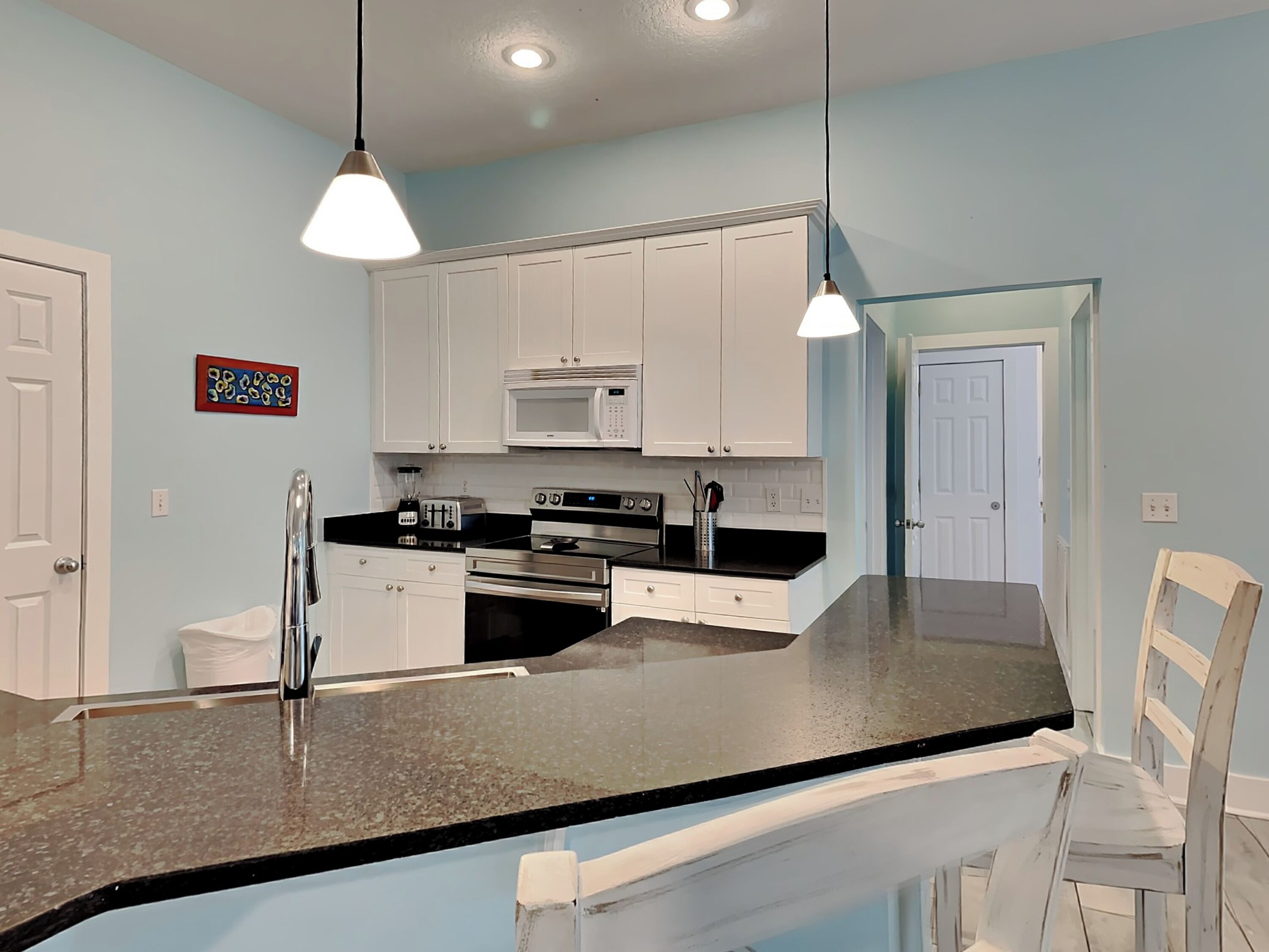 A modern kitchen with white cabinets, a black countertop, stainless steel appliances, and pendant lighting.