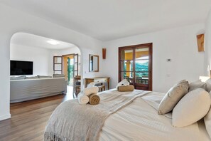 A bedroom with a bed, a TV, a desk, and a view of the outdoors.
